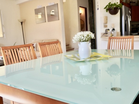 Departamento en venta en centro cancún - Comedor con mesa de cristal y sillas de madera. Al fondo una sala de estar