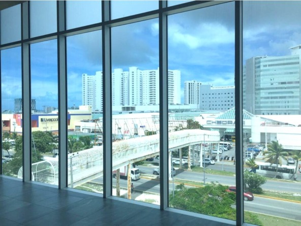 oficina en venta en cancún centro - ventanal de cristal con vista hacia plaza comercial y edificios al fondo