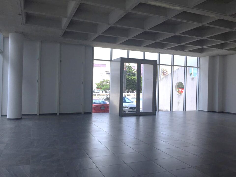 oficina en venta en cancún centro - Entrada a local comercial amplio con piso de loseta gris, techos altos y ventanales de cristal que dan a la calle.